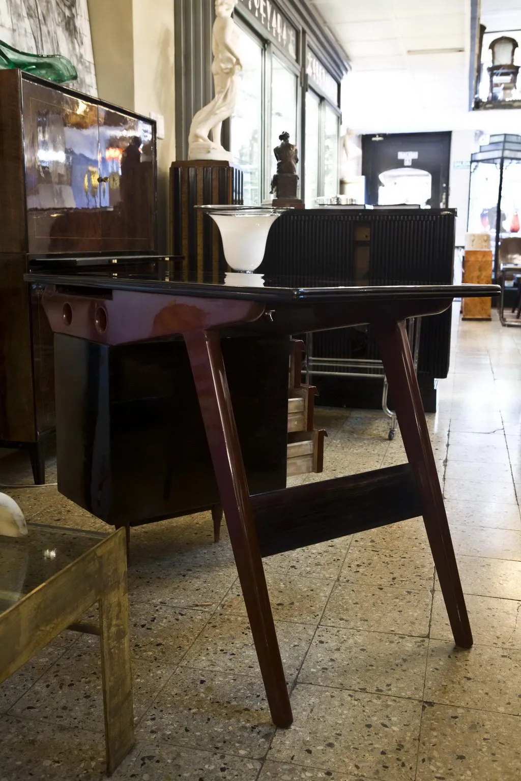 Escritorio antigo de madeira com superfície preta e pernas elegantes, decorado com um objeto branco