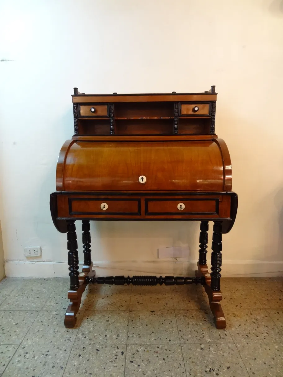 Scrivania antica in legno con scaffale e cassetti decorativi in ​​un ambiente semplice.