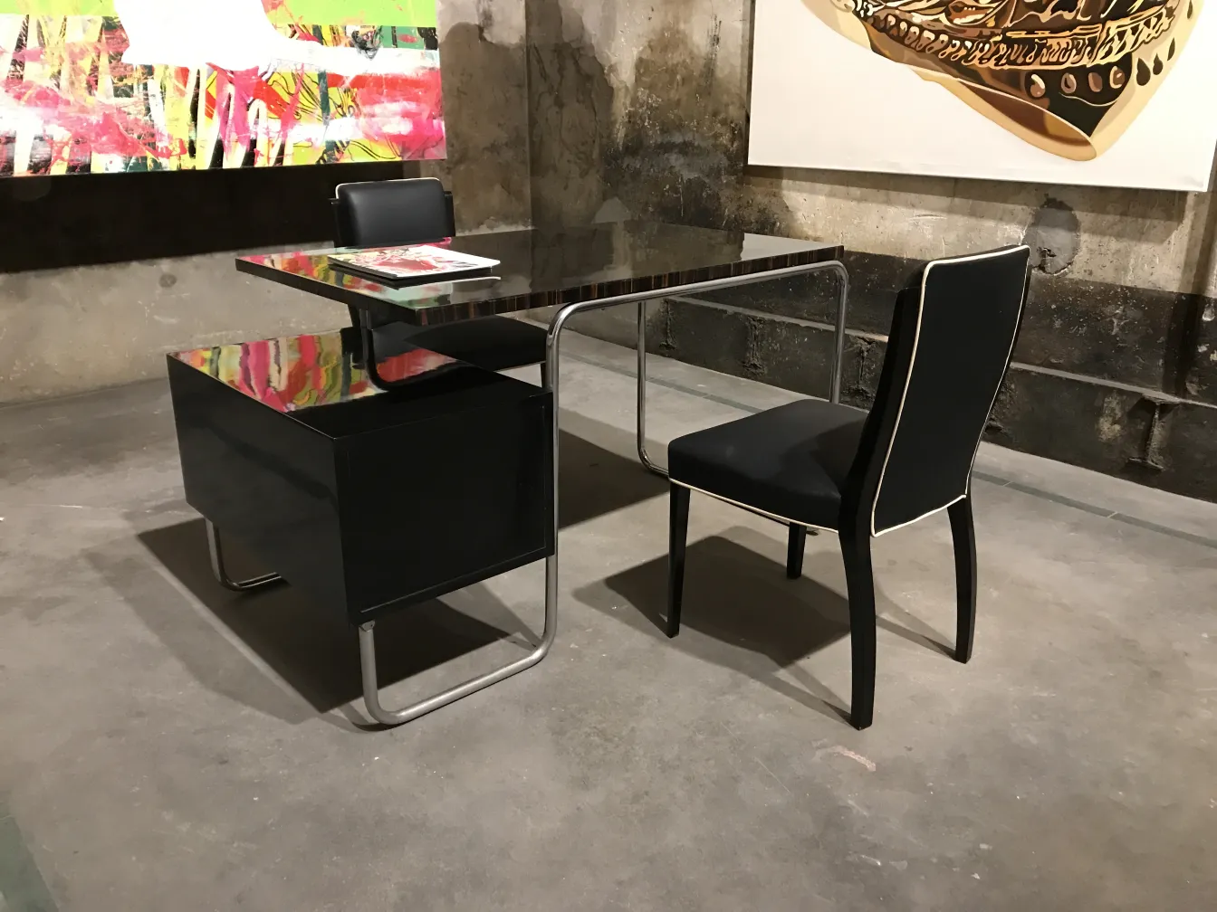 Modern antique desk with glossy finishes and black chair in an industrial setting.