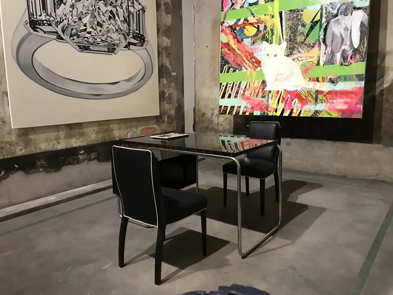 Antique desk with black chairs, modern art in the background.