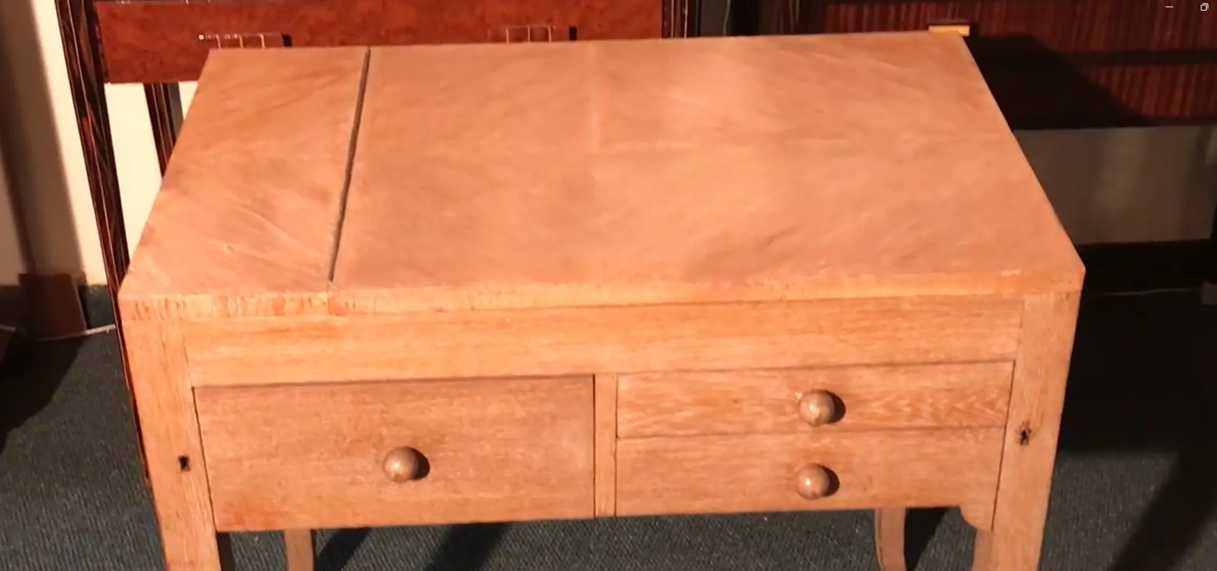 Escritorio antiguo de madera clara con dos cajones redondeados en un ambiente suave.