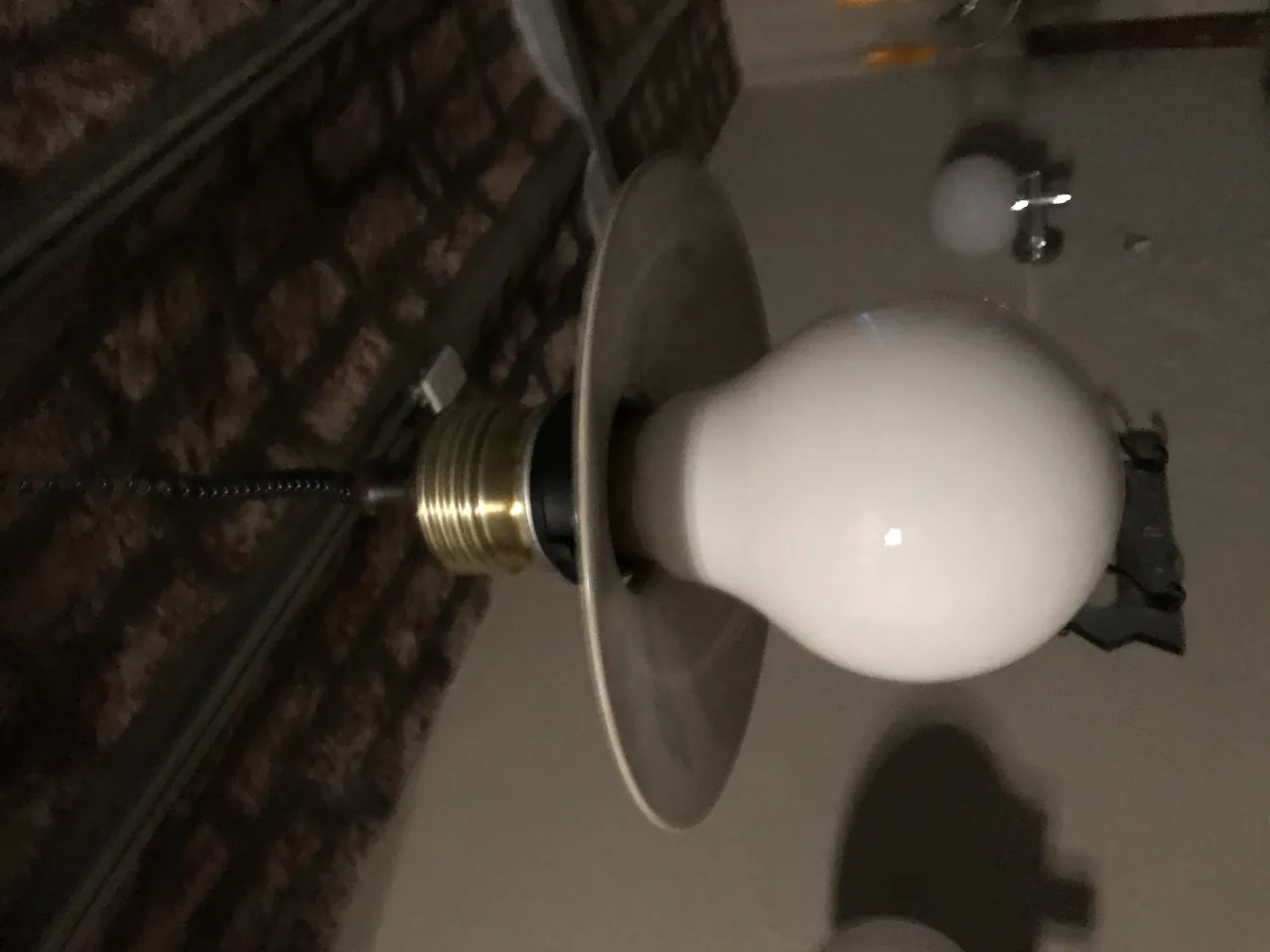 Lampada a sospensione antica con bulbo bianco su sfondo di mattoni.