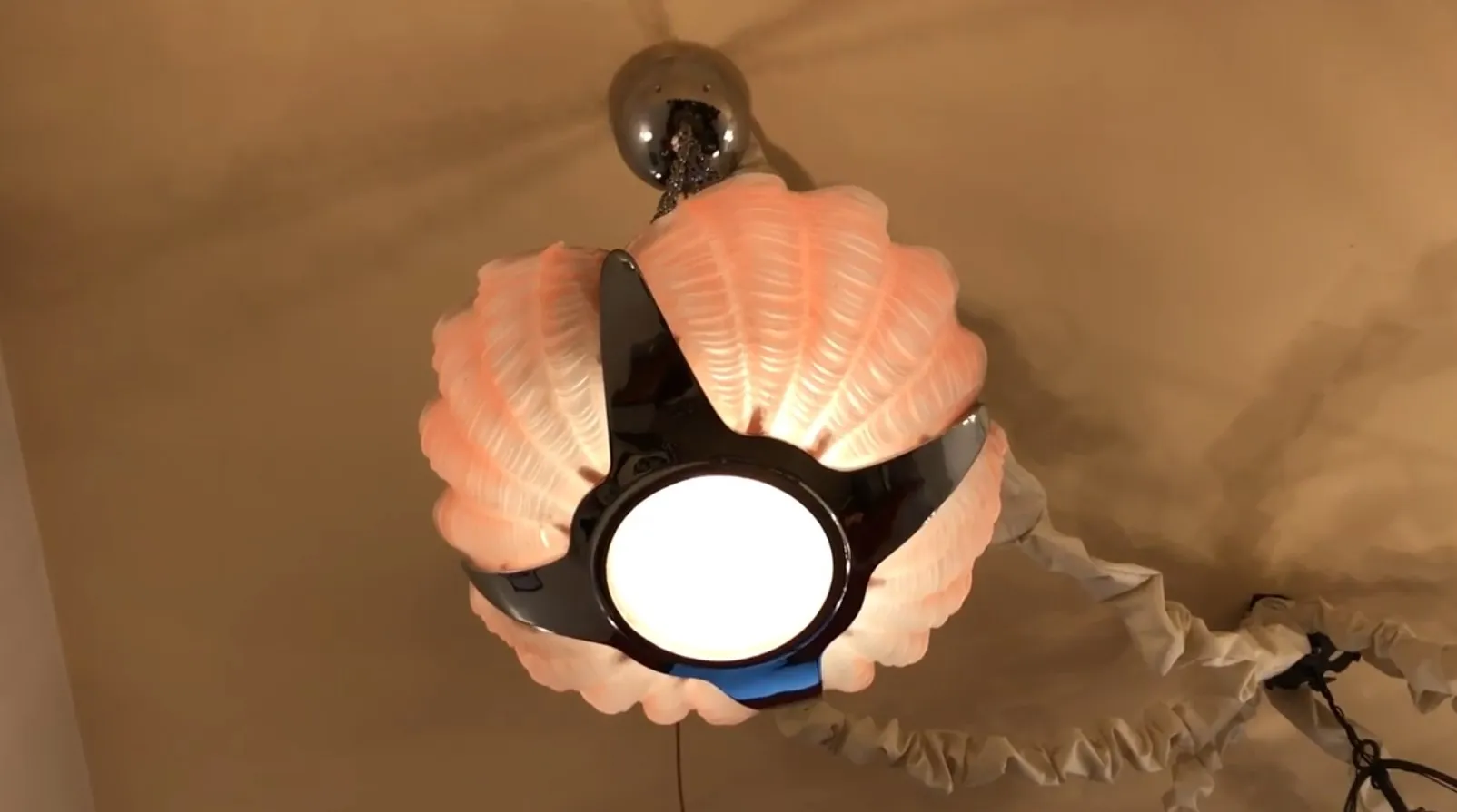 Lampada a sospensione antica con design a conchiglia e luce centrale brillante.