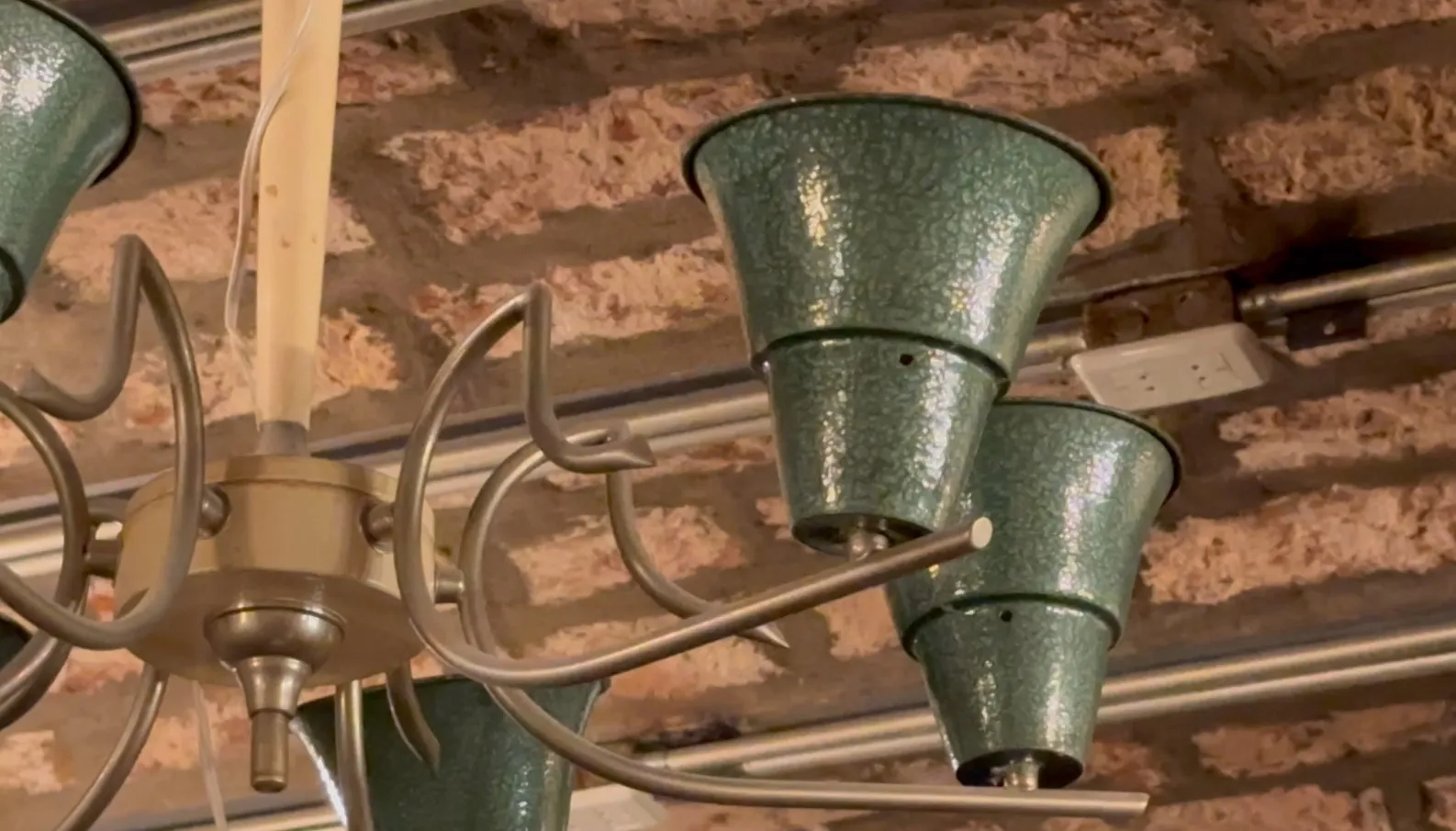 Antica lampada a sospensione di colore verde brillante in un ambiente rustico con muri in mattoni.