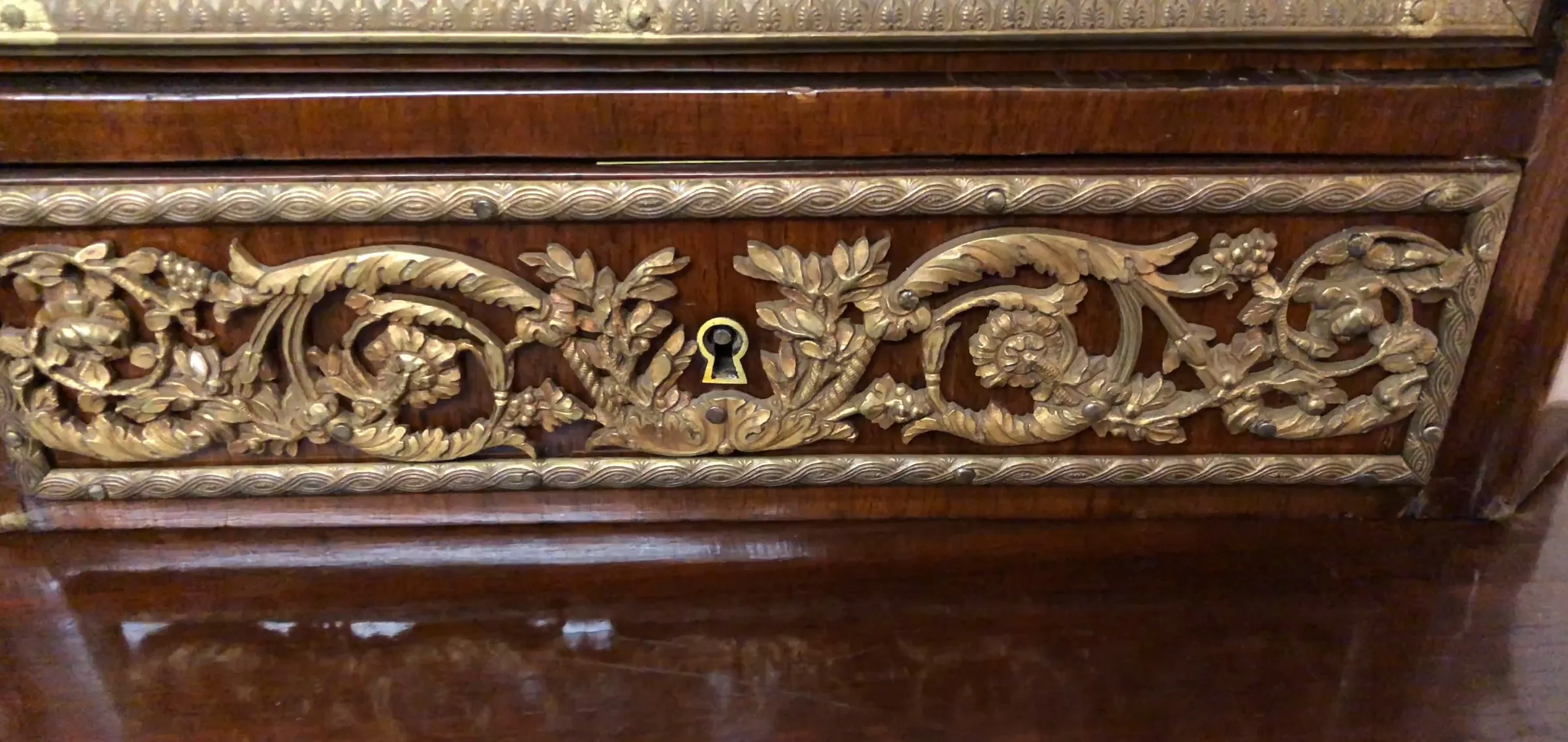 Escritorio antiguo de madera con detalles en relieve y una cerradura dorada.