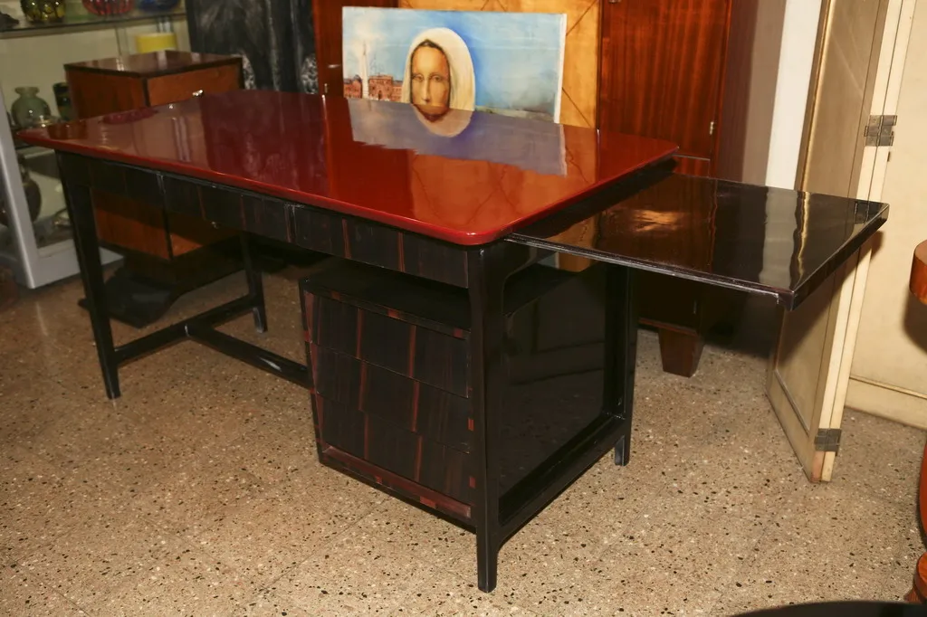 Escritorio antiguo con superficie roja y lateral negro en ambiente clásico.