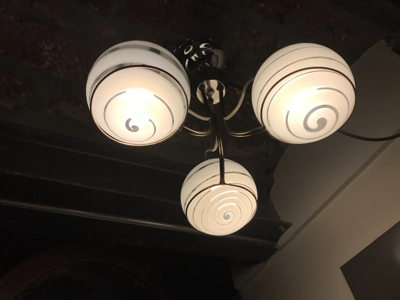 Lampada a sospensione antica con tre lampadine bianche e dettagli decorativi a spirale