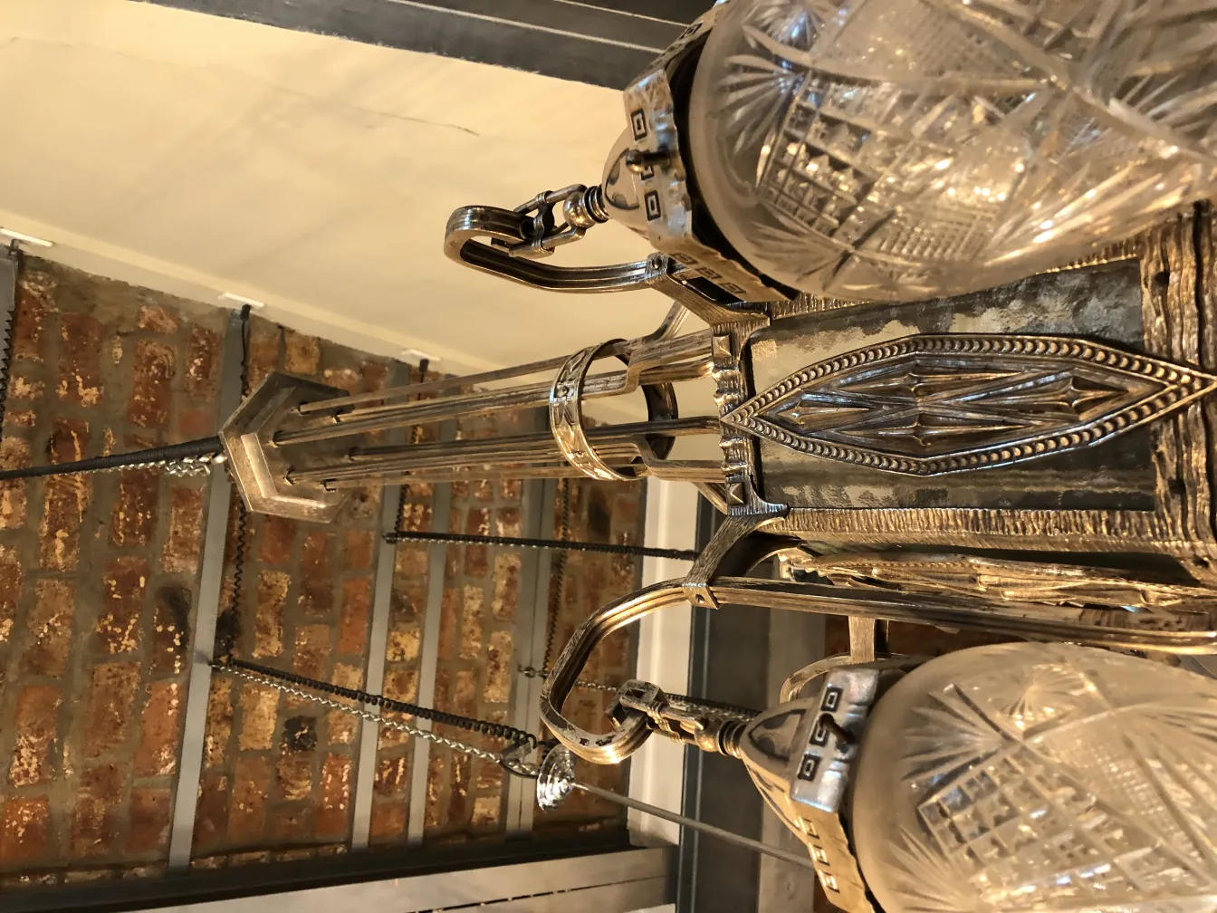 Antique hanging lamp with elegant crystals, suspended in a cozy setting with brick walls.