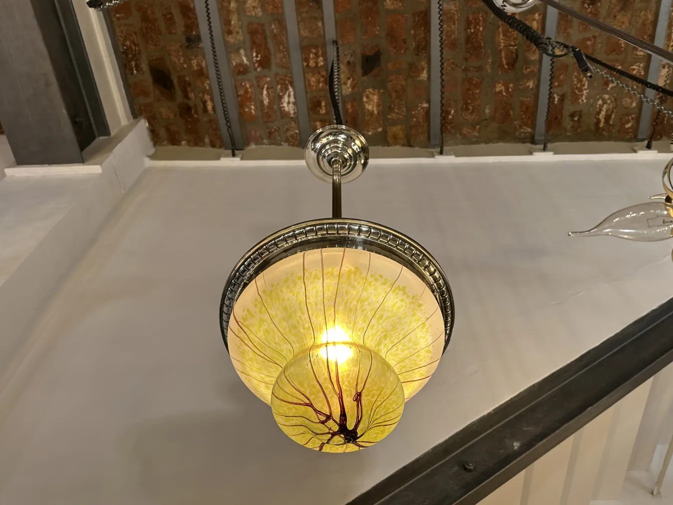 Lâmpada de teto antiga de cor âmbar com detalhes elegantes, iluminando um espaço. Fundo de tijolo visível.