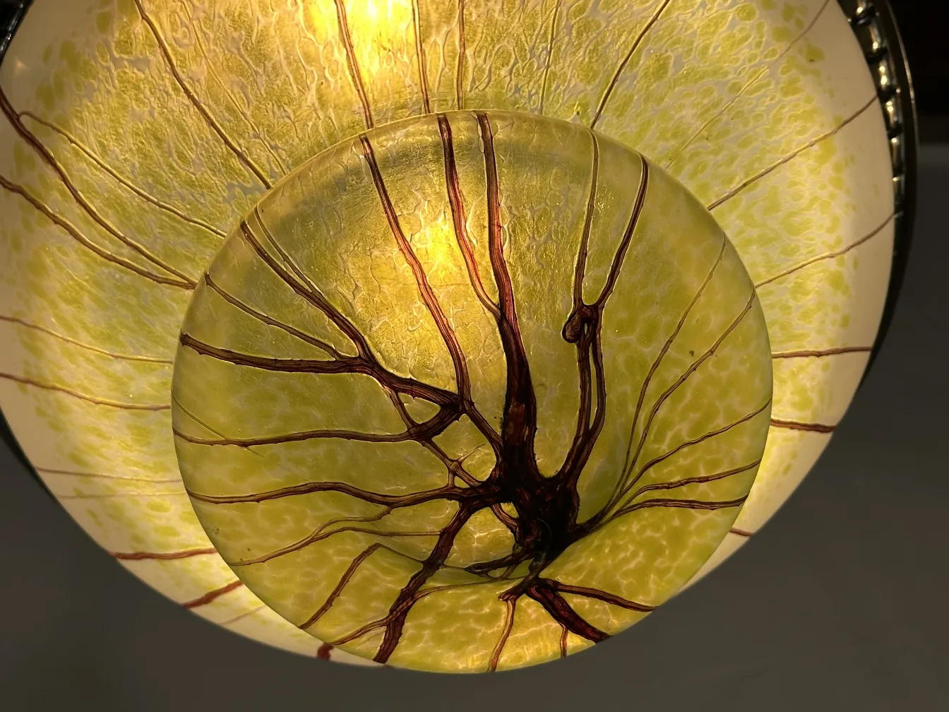 Lámpara de techo antigua de vidrio con diseño natural en tonos amarillos, iluminando suavemente el ambiente.