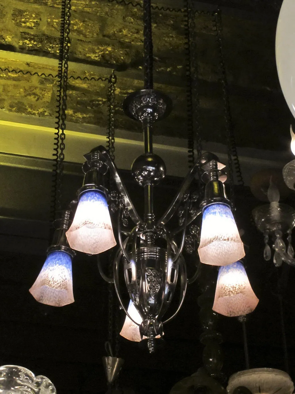 Lampada a sospensione antica con bracci in vetro colorati che illuminano uno spazio scuro.