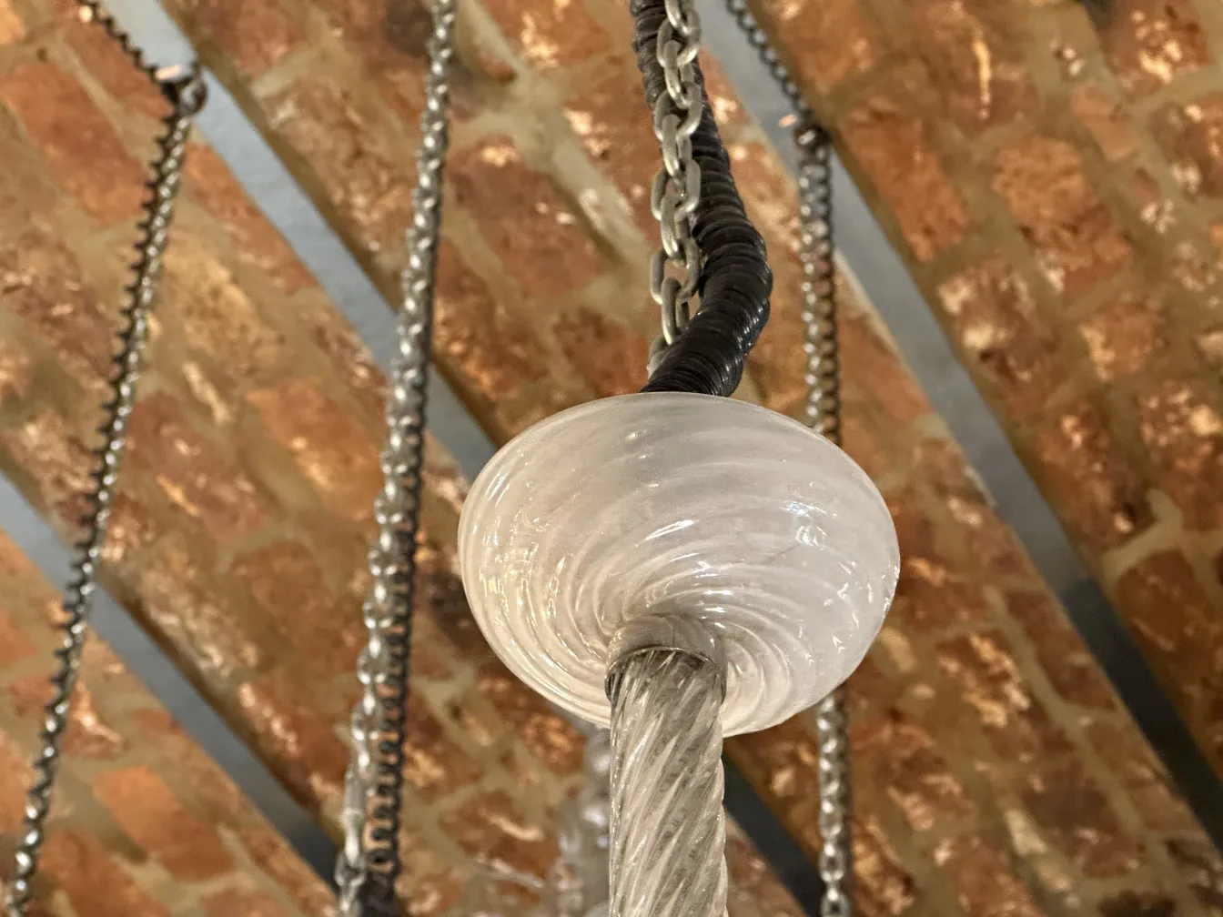 Antike Hängelampe mit Metallkette und Glaselementen, in rustikaler Umgebung hängend.