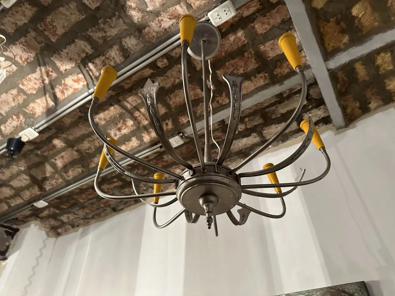 Lampada a sospensione antica con design elegante e bracci curvi su uno sfondo di soffitto in mattoni.