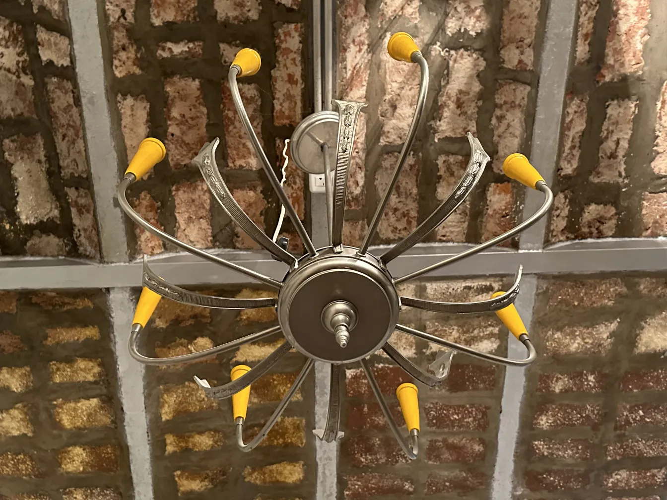 Antike Hängelampe mit gebogenen Metallarmen und gelben Details, die eine rustikale Umgebung beleuchtet.