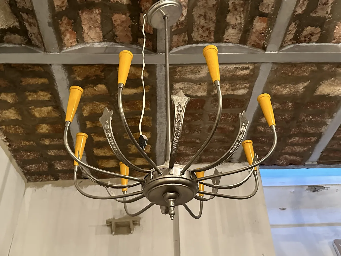 Antica lampada a sospensione con dettagli decorativi e capsule arancioni, appesa a un soffitto in mattoni a vista.