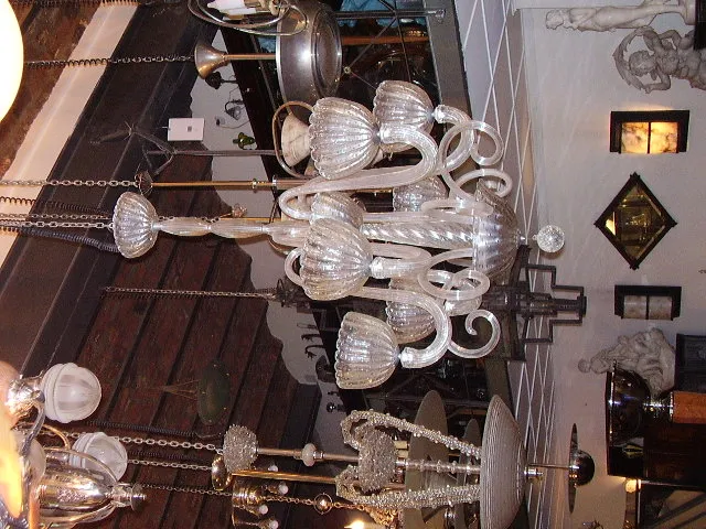 Antica lampada a sospensione in vetro con più bracci e dettagli intricati, in un ambiente decorativo.