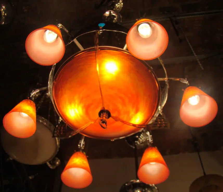 Lampada a sospensione antica con sei paralumi arancioni luminosi in un ambiente scuro.