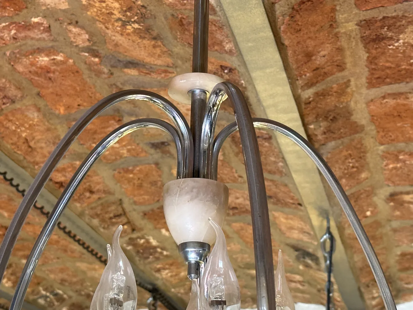 Antique hanging lamp with curved arms and decorative glass in an exposed brick setting.