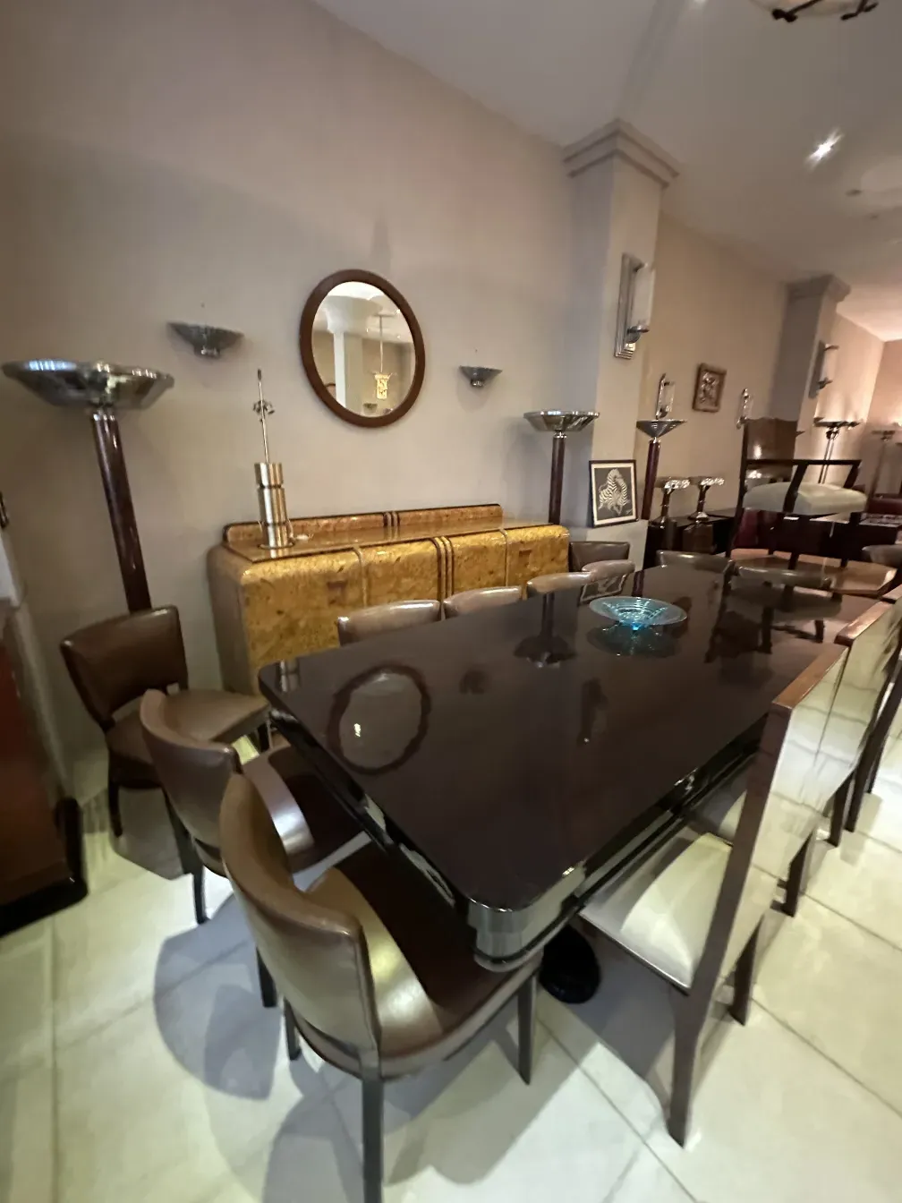 Aparador antigo com detalhes elegantes em um ambiente moderno, cercado de cadeiras e espelhos.