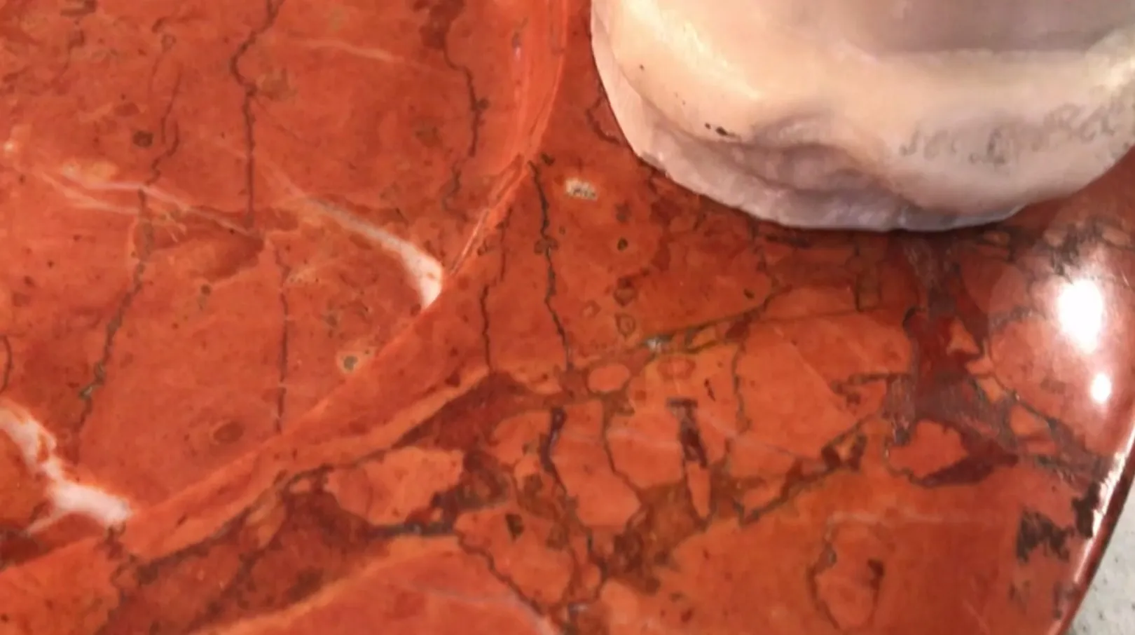 Cinzeiro de pé antigo com detalhes decorativos sobre a superfície vermelha.