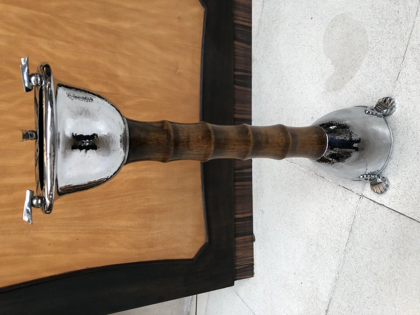 Cinzeiro de pé antigo com acabamento brilhante e detalhes decorativos em um ambiente neutro.