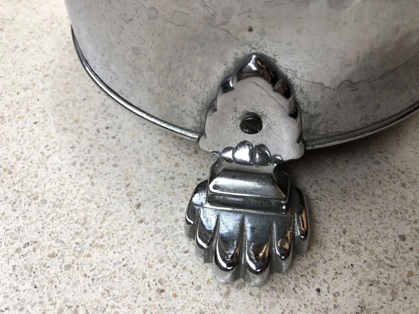 Cenicero de pie antiguo con una base decorativa en forma de garra en una superficie clara.