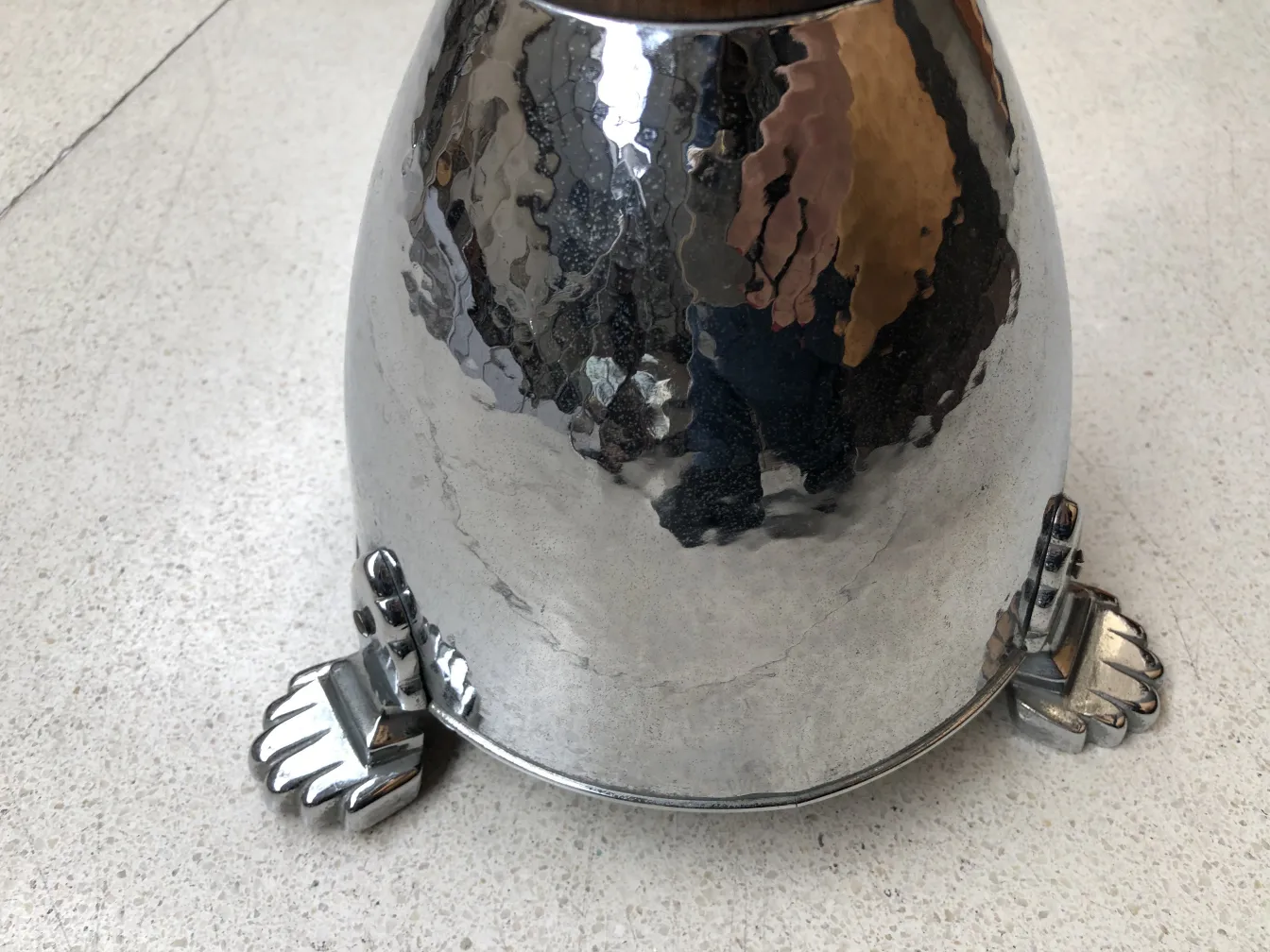 Старая стоячая пепельница с блестящей отделкой и декоративными подставками на светлой поверхности.