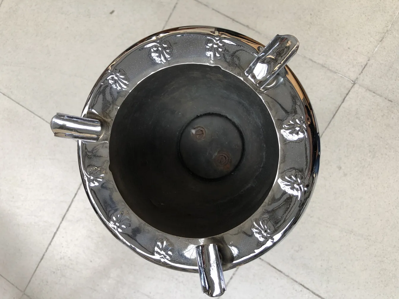 Cendrier sur pied ancien avec un design de feuilles argentées, vu de dessus dans un cadre neutre.