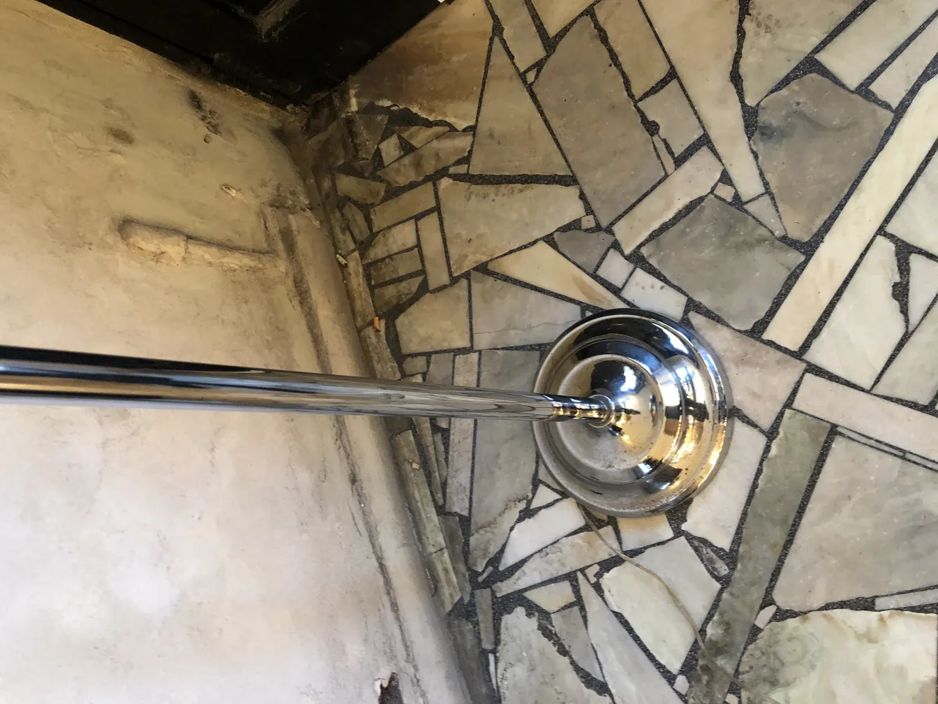 Antike Stehleuchte mit glänzender Metallbasis, neben einem Mosaikboden.