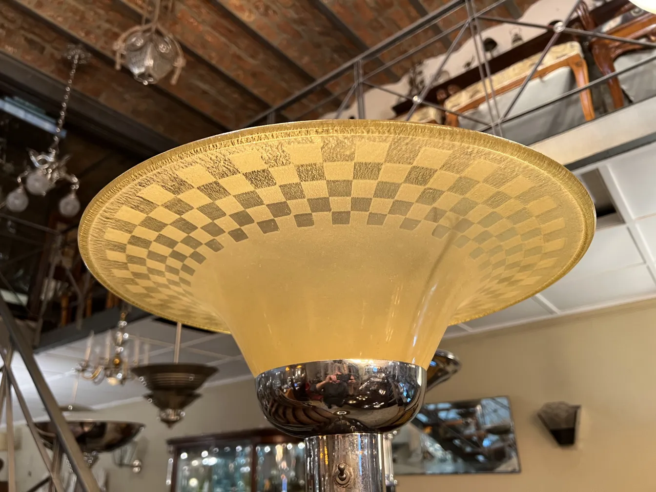 Lampe de sol ancienne avec abat-jour à carreaux, entourée de divers objets décoratifs et meubles.