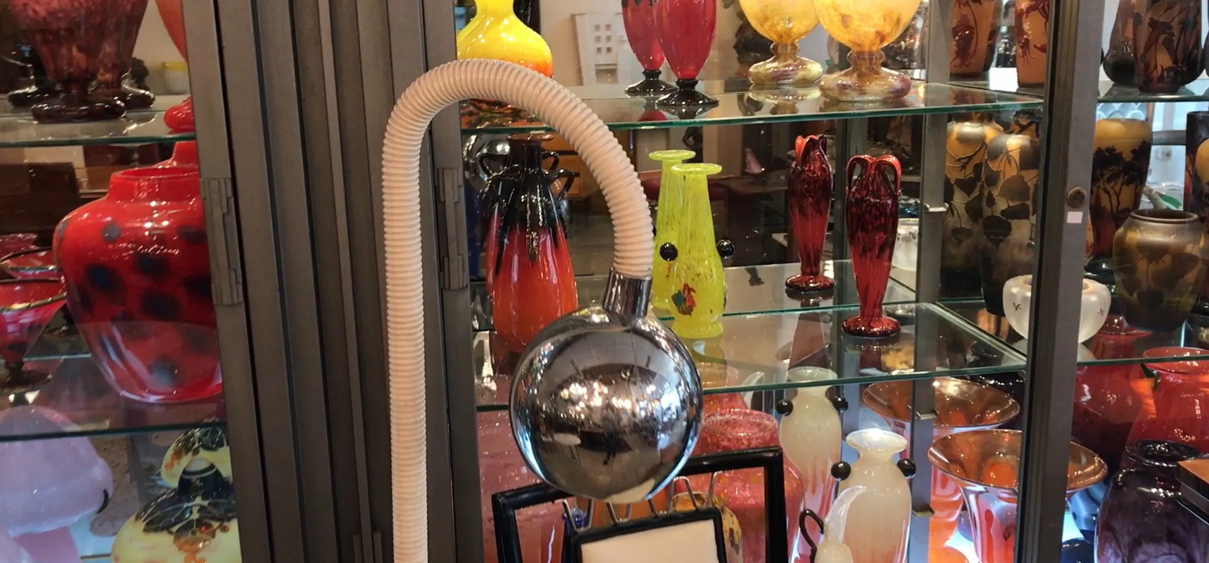 Luminária de pé antiga com base esférica brilhante entre vasos coloridos.