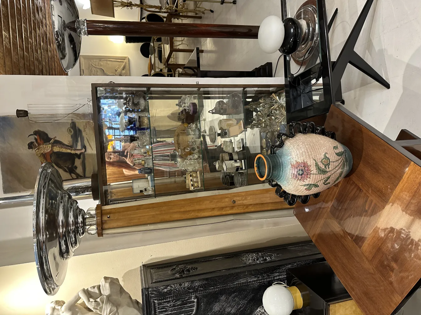 Lámpara de pie antigua con base de madera y pantalla brillante, rodeada de antigüedades.