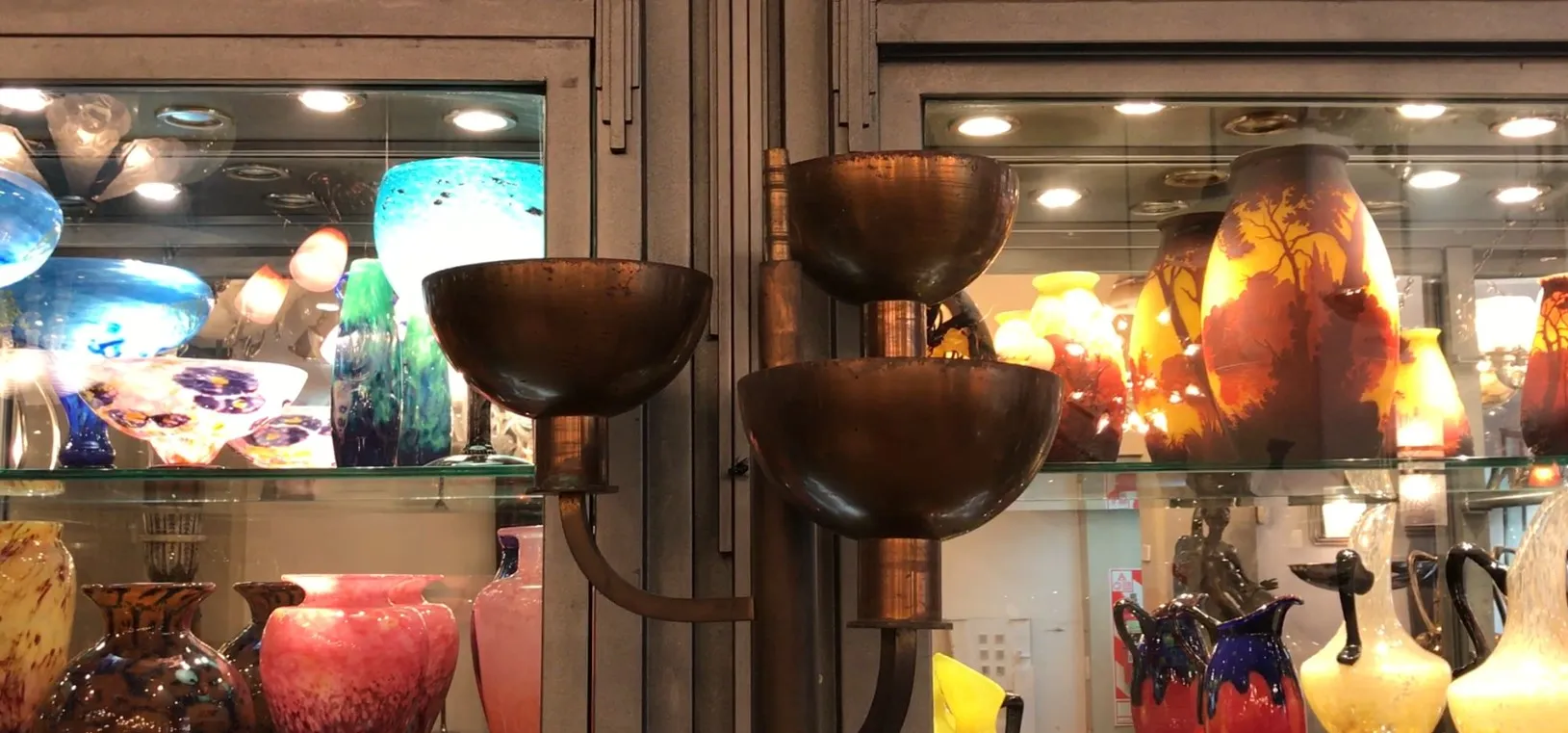 Lámpara de pie antigua con dos aberturas, en un ambiente con jarrones de colores vivos.