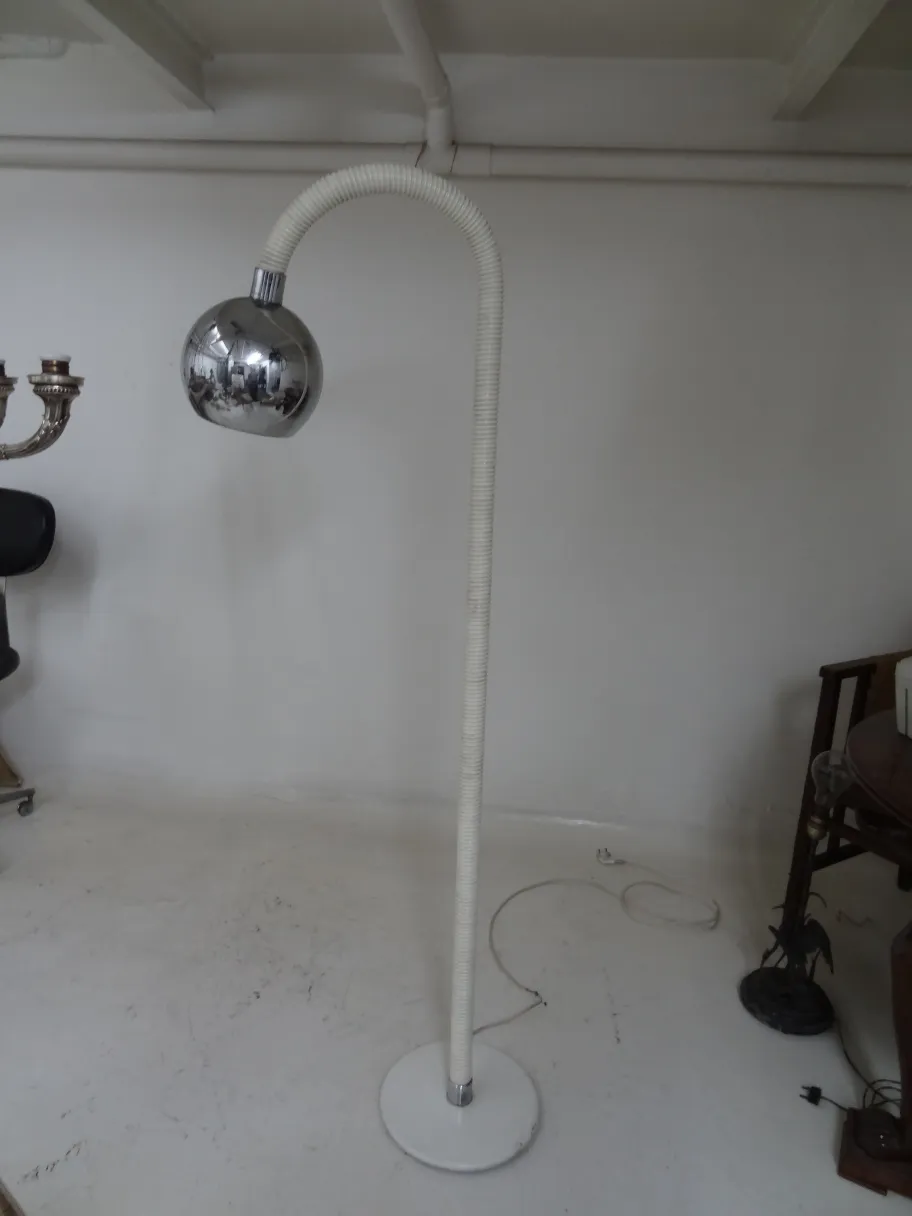 Lampada da terra antica con braccio curvo e base rotonda in uno sfondo minimalista.