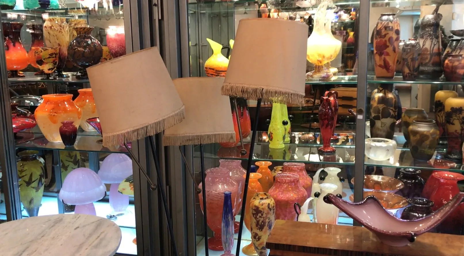 Luminária de pé antiga com abajour claro em meio a vasos coloridos.