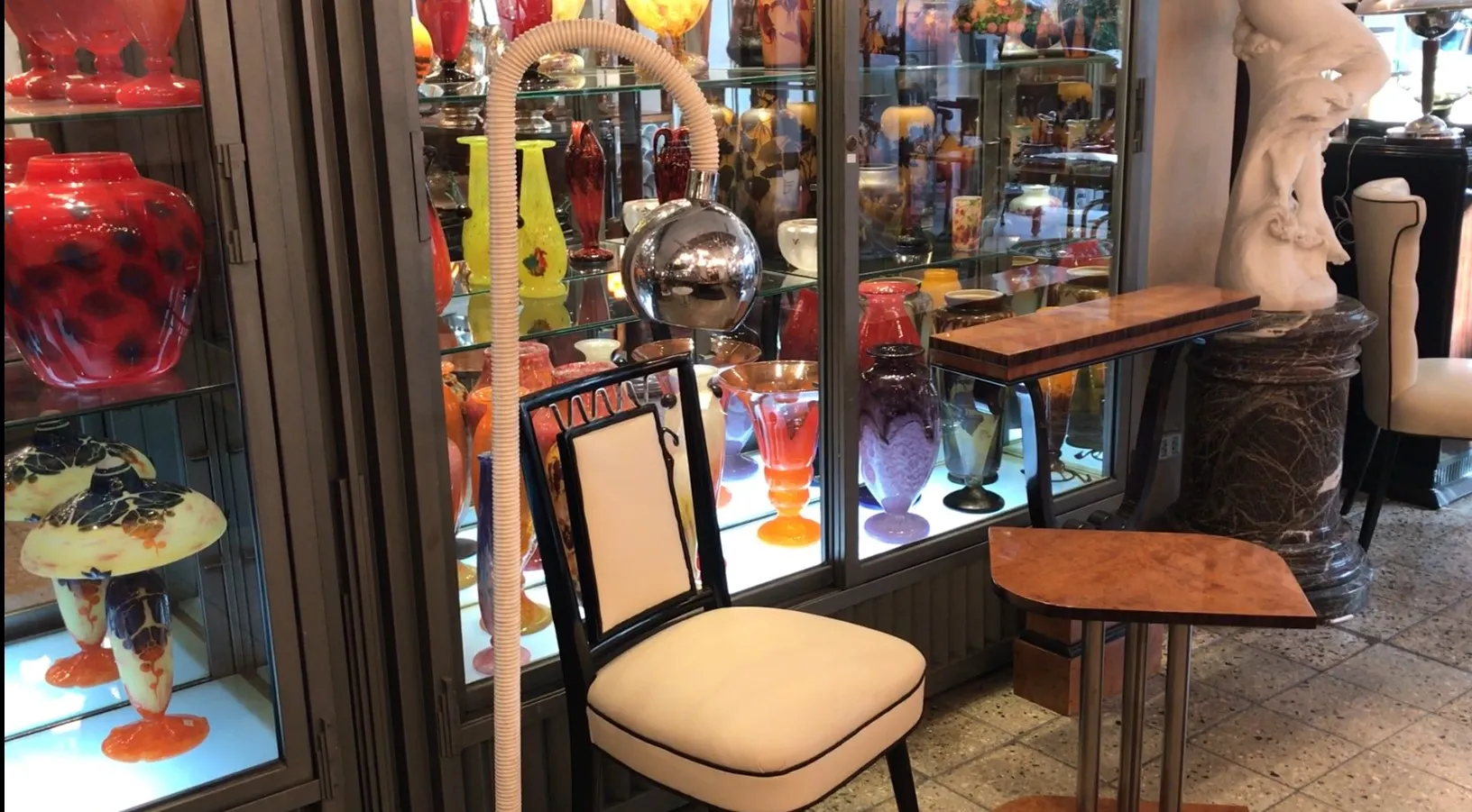 Lampada da terra antica con design elegante, accanto a una sedia bianca e decorazioni colorate sullo sfondo.