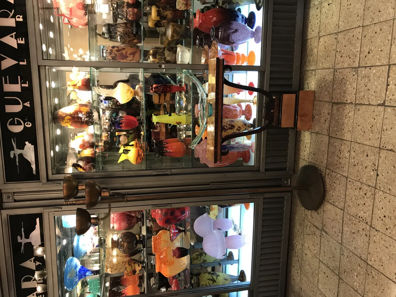 Alte Stehleuchte mit klassischem Design und zwei Leuchten, vor einem mit Glaswaren gefüllten Galeriewand.