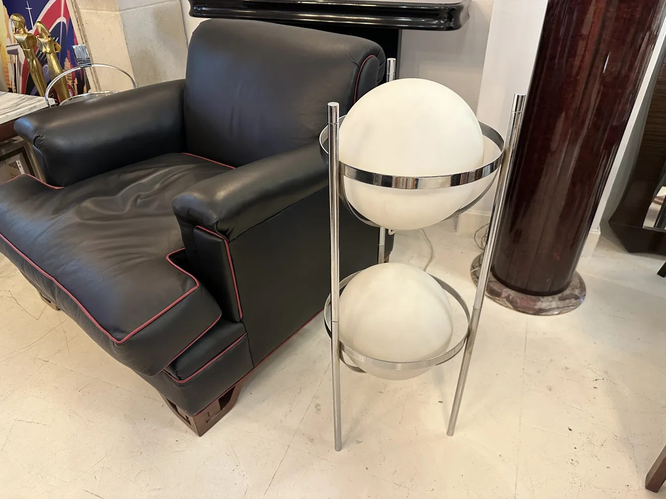 Lámpara de pie antigua con dos esferas blancas en un soporte metálico, decorando una sala con un sofá negro.