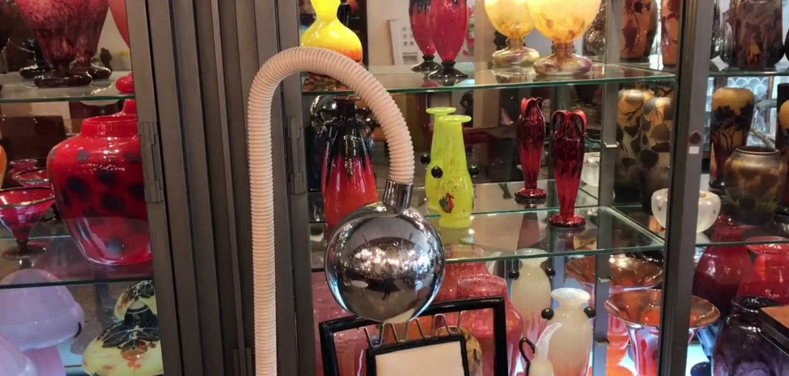 Luminária de pé antiga com estrutura brilhante, adornada entre outras antiguidades coloridas.