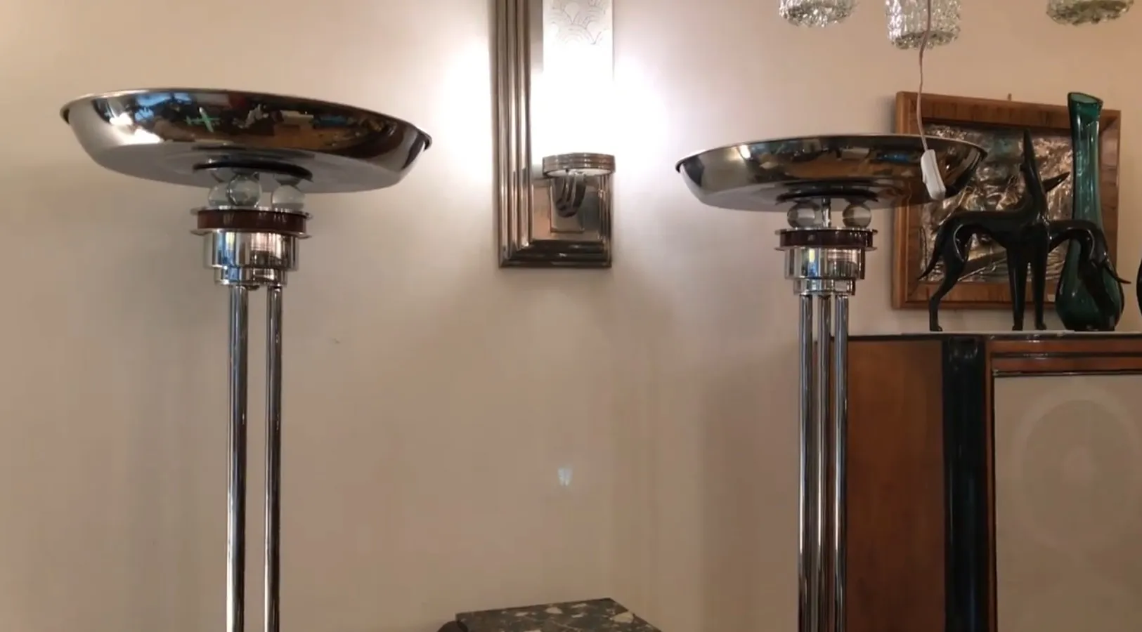 Vista de 2 lâmpadas de piso antigas com acabamento brilhante, em um ambiente decorativo com arte na parede e outros objetos.