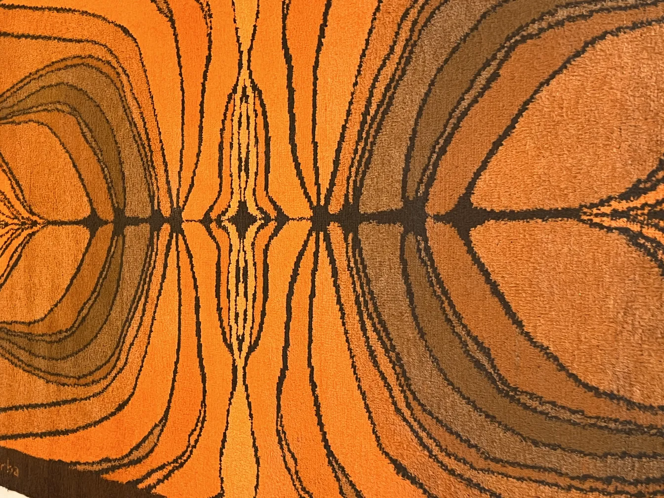 antiker Teppich mit geometrischem Muster in orange und braun, das Wärme in den Raum bringt.