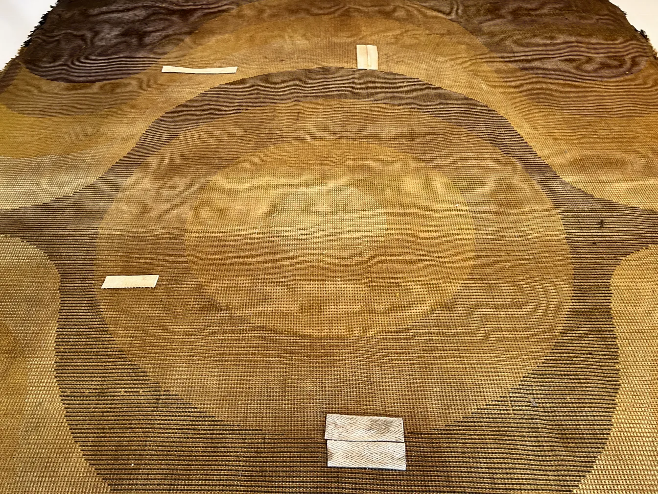 Tapis ancien avec des motifs géométriques dans des tons bruns et beiges, dans une atmosphère chaleureuse.