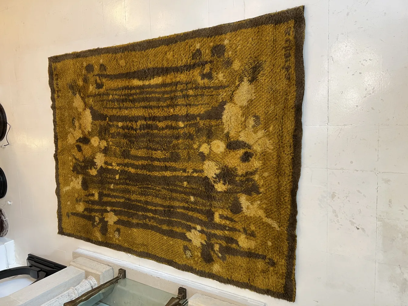 Alter dekorativer Teppich in ockerfarbe an einer weißen Wand