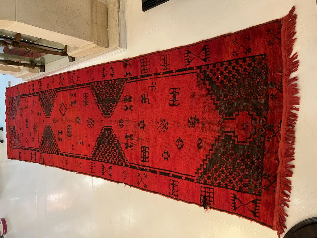 Tappeto antico rosso con motivi geometrici su un pavimento elegante.