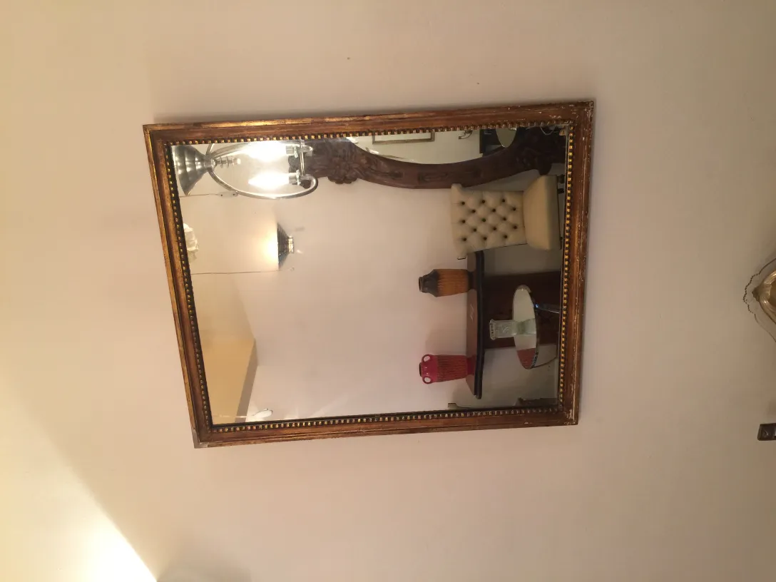 Miroir ancien avec cadre décoratif sur un mur blanc, reflétant un environnement élégant.