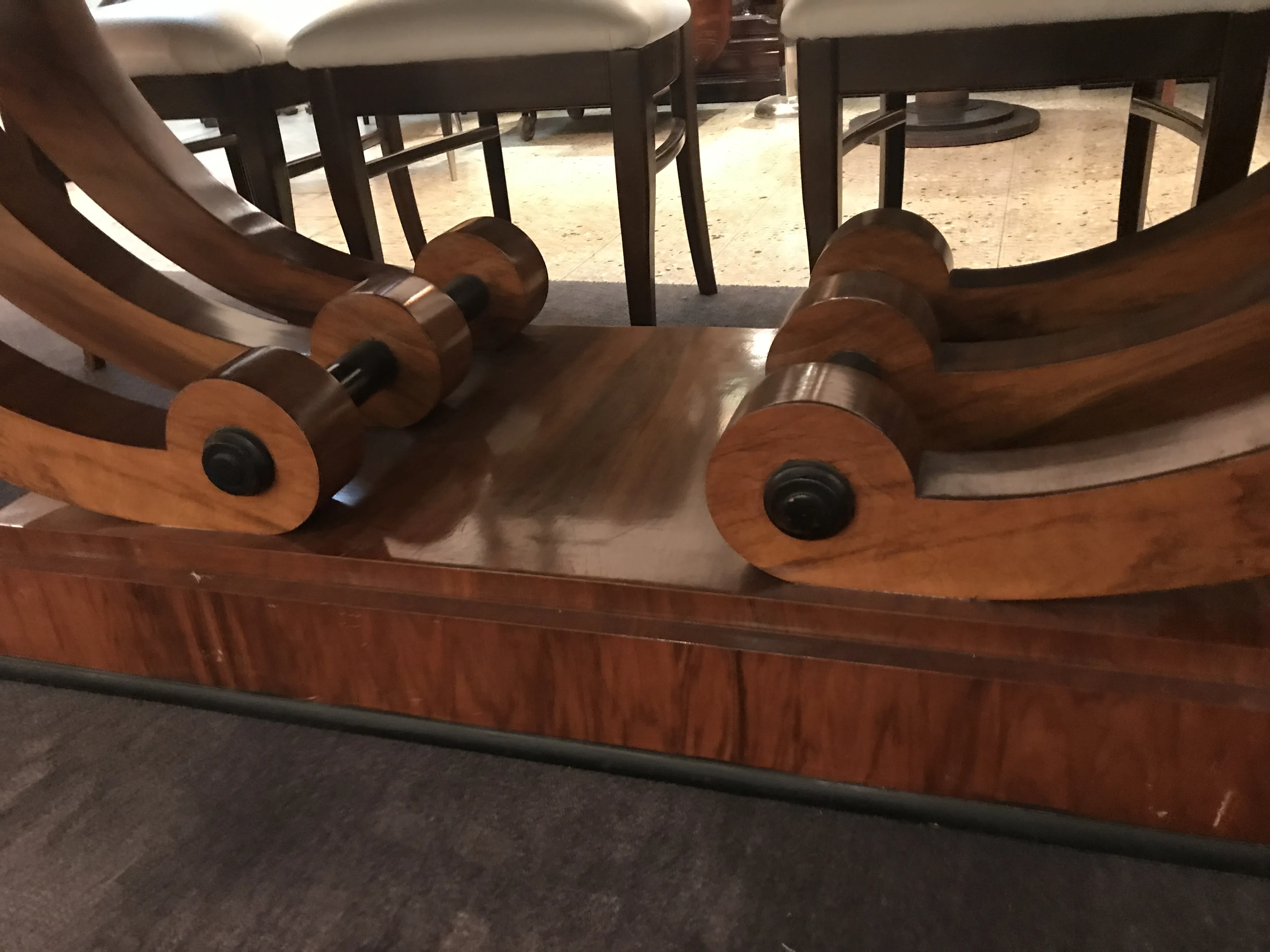 Mesa de comedor antigua para 10 personas con base decorativa, sillas al fondo.