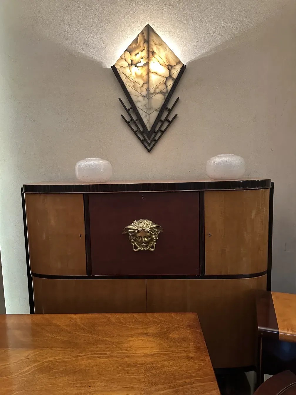 Estante de livros antigo com um design único, adornado com um detalhe dourado em um fundo neutro.