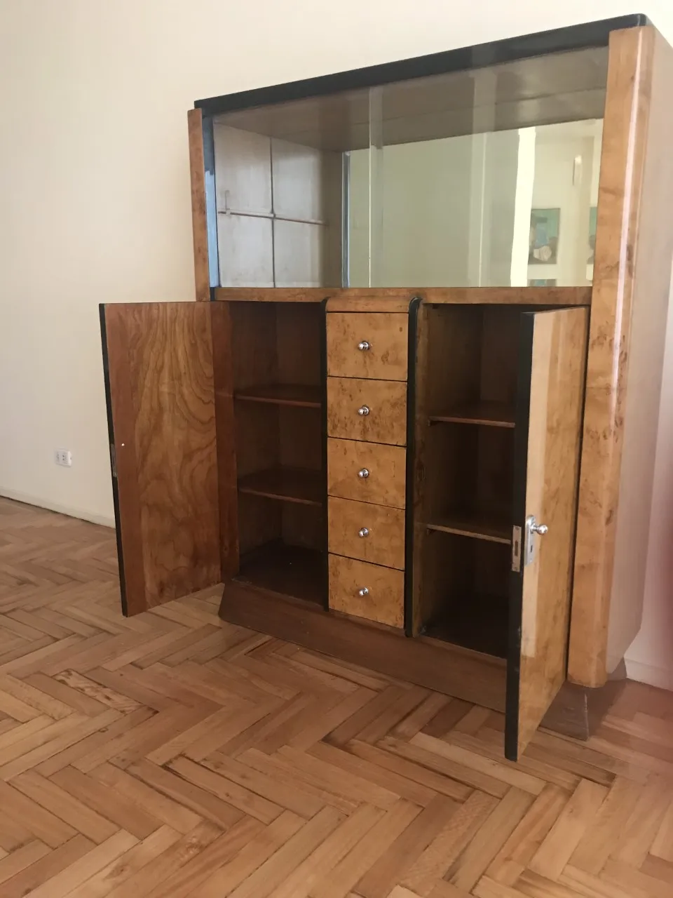 Biblioteca antigua con espejo, cajones y puertas abiertas en un entorno minimalista.