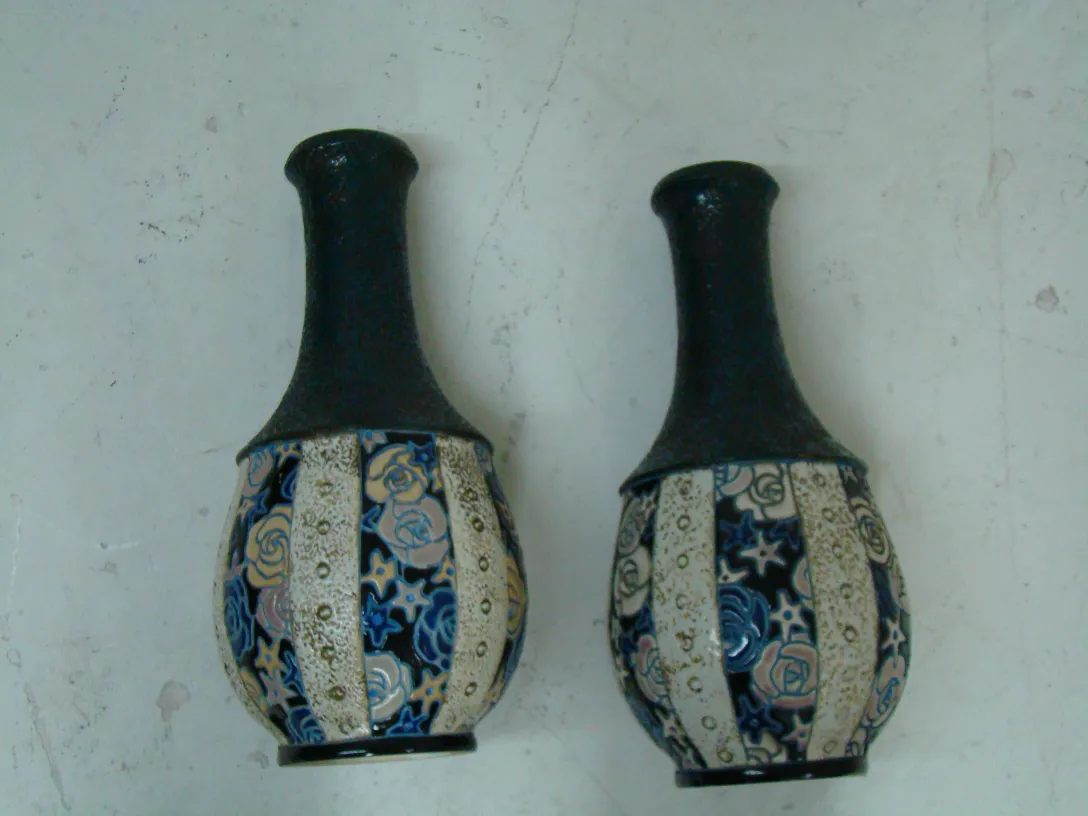 due vasi in ceramica antichi con decorazione floreale colorata. Sullo sfondo, un ambiente neutro.