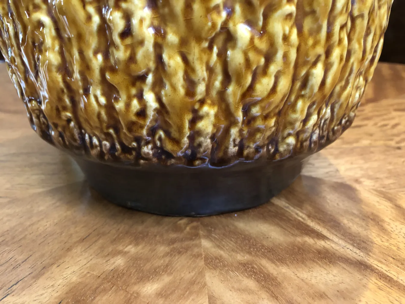 Vaso de cerámica âmbar antigo com textura irregular em uma mesa de madeira.